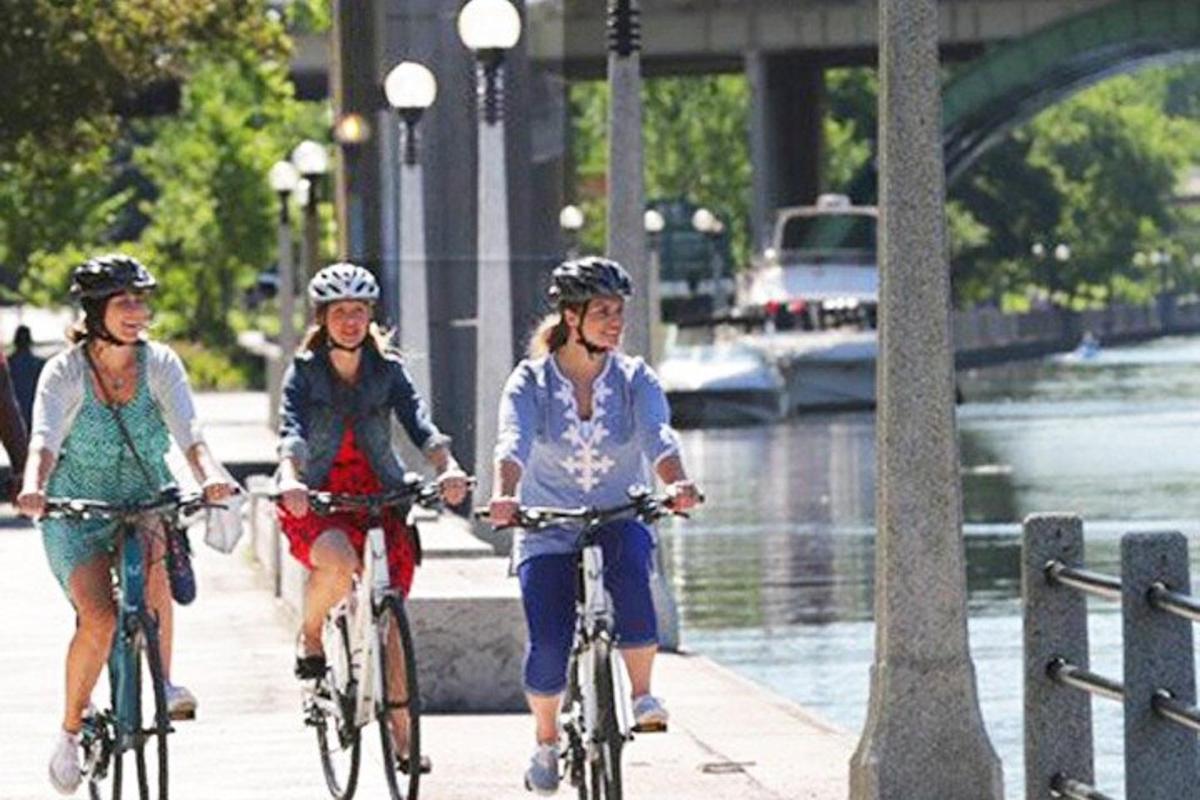 three women riding bikes down a sidewalk next to a river