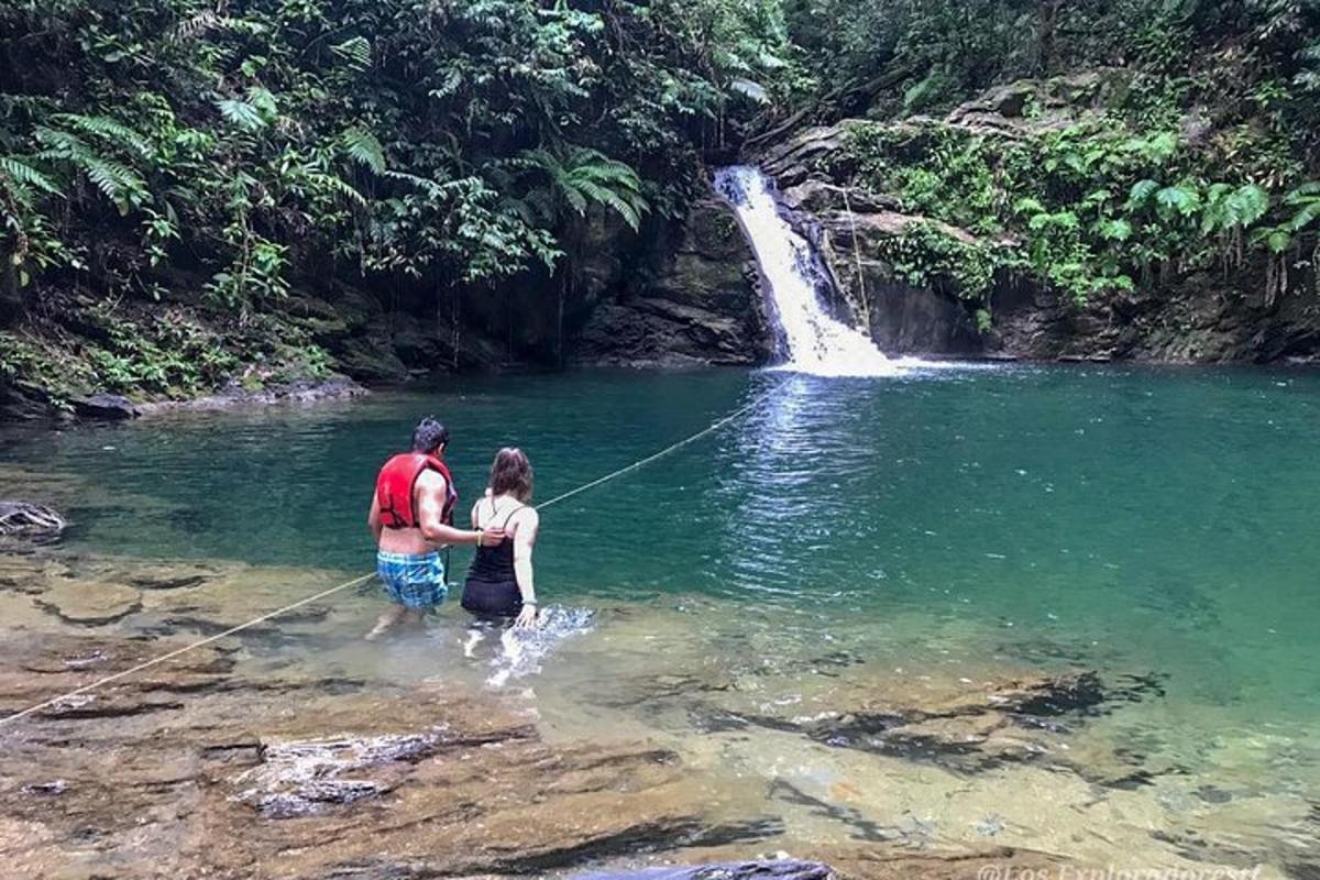 a man and a girl standing in the water in front of a waterfall