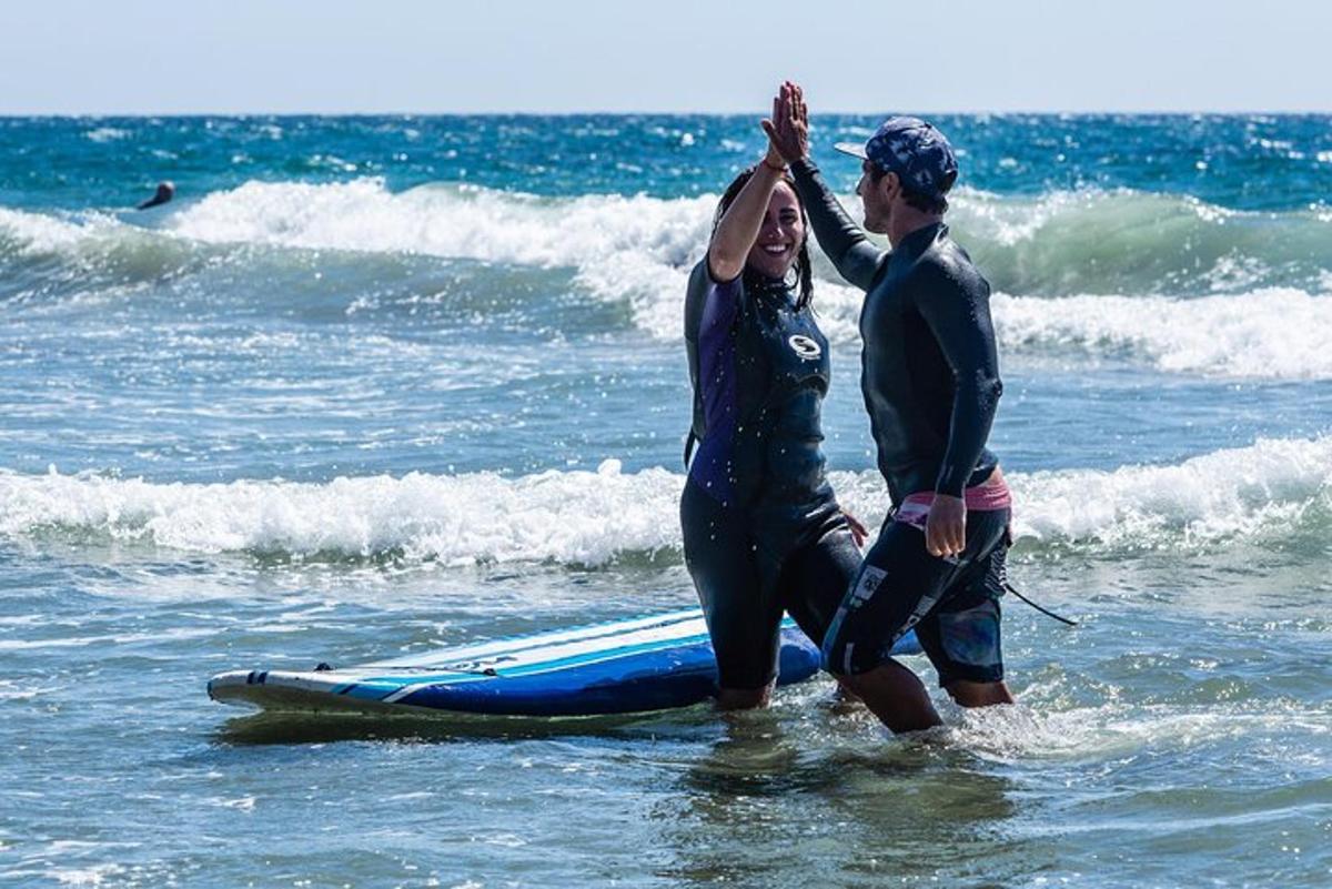 Un hombre y una mujer de pie en el océano con una tabla de surf.