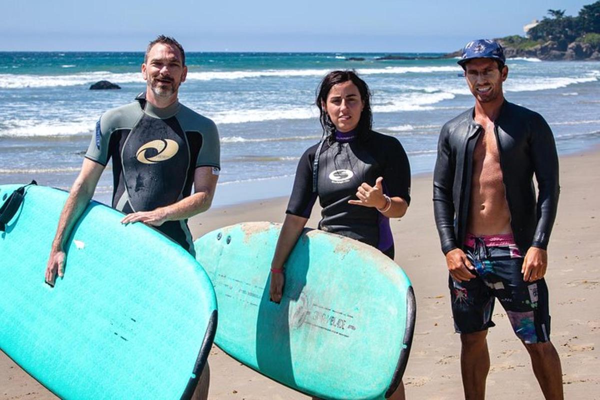 três pessoas em pé na praia com suas pranchas de surfe