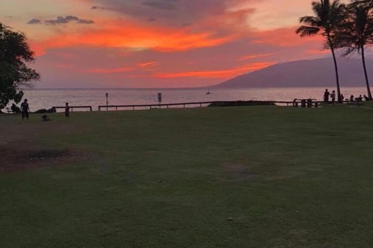 matahari terbenam di atas lautan dengan orang berjalan di pantai