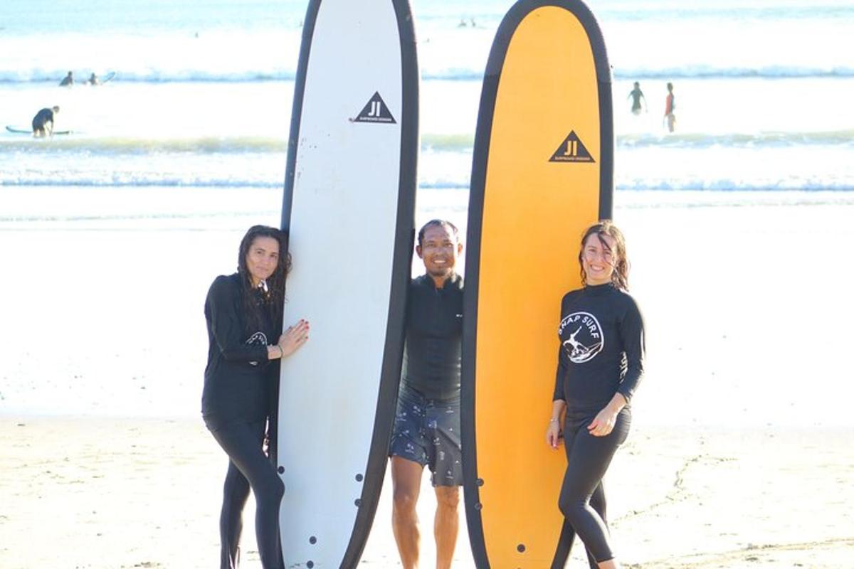 tatlong tao na nakatayo sa dalampasigan na may mga surfboard