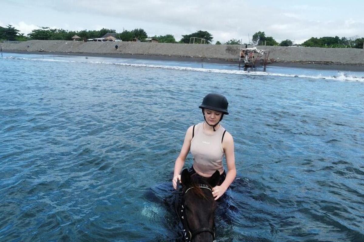 Una mujer está parada sobre un caballo en el agua.