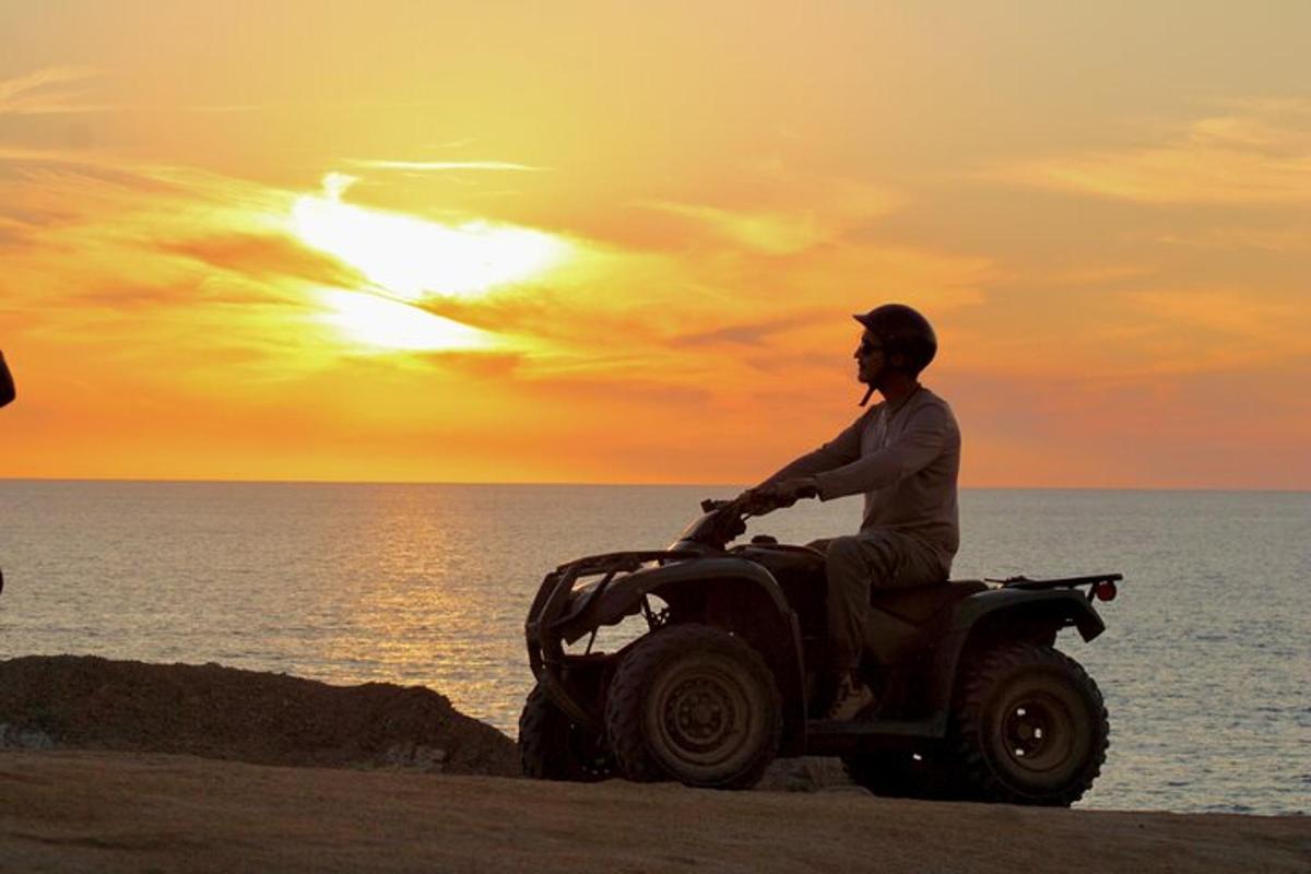un bărbat care merge pe un ATV pe plajă la apus