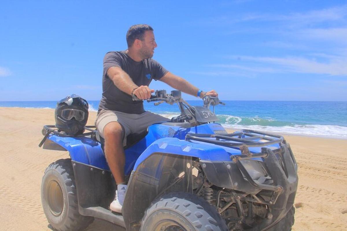 Un hombre sentado en un vehículo todo terreno en la playa.
