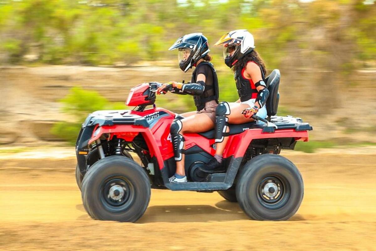 Dos personas viajando en un vehículo rojo de cuatro ruedas en la carretera.