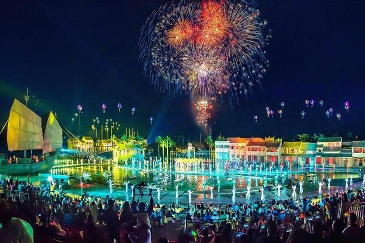 uma multidão de pessoas em pé em frente a uma fonte com fogos de artifício