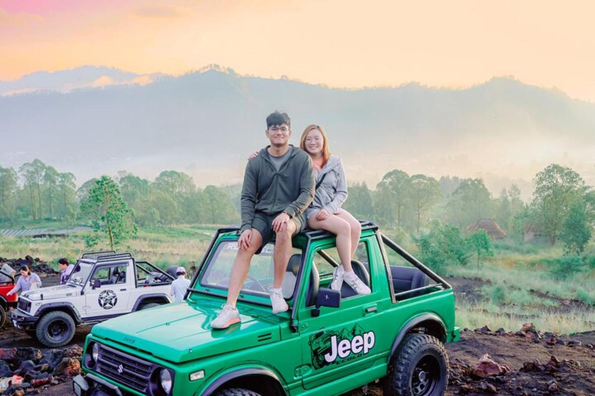 a man and woman sitting on the hood of a green jeep