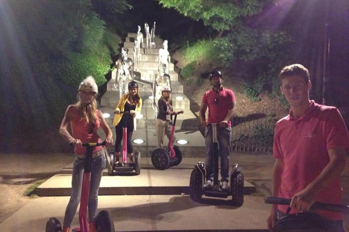 Skupina lidí jedoucích na segwayích před památníkem