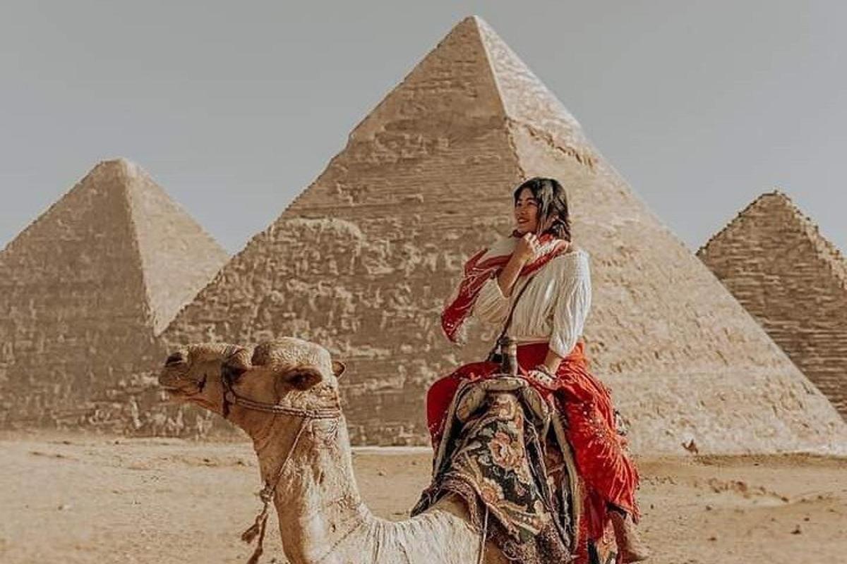 uma mulher montando um camelo em frente às pirâmides