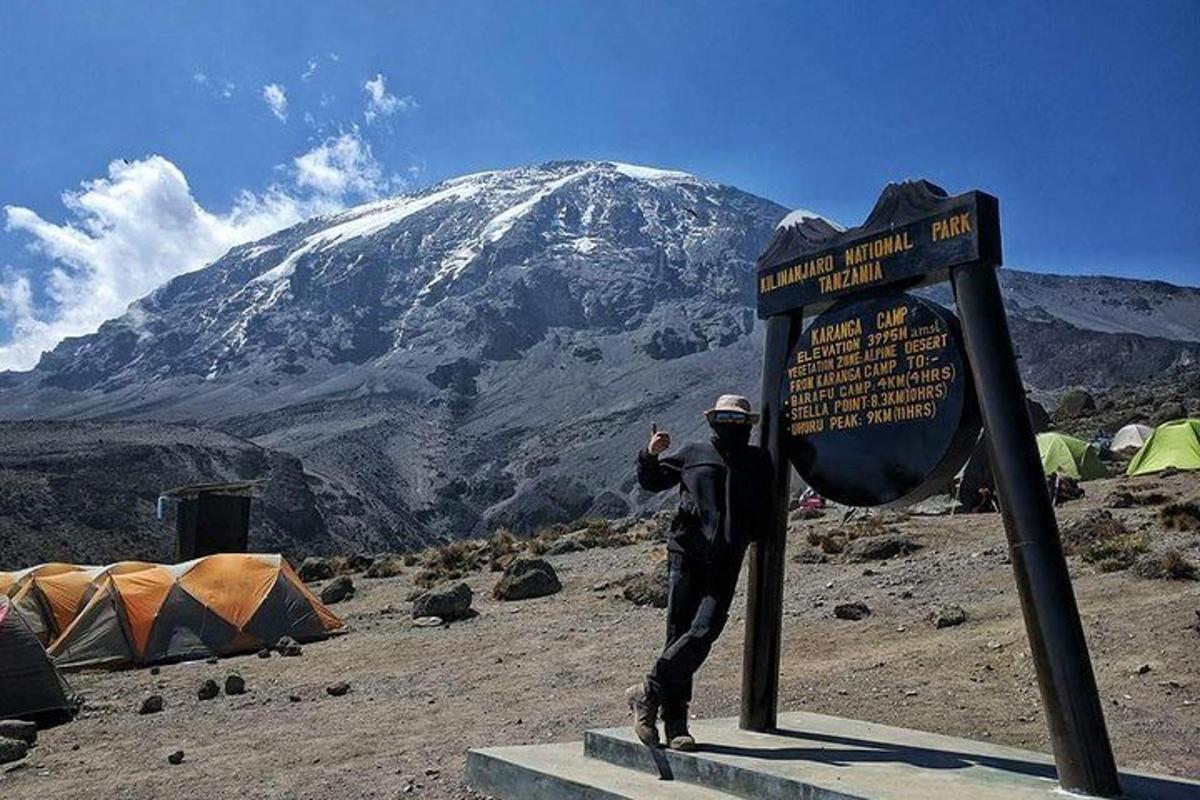 Un hombre parado junto a un cartel frente a una montaña.
