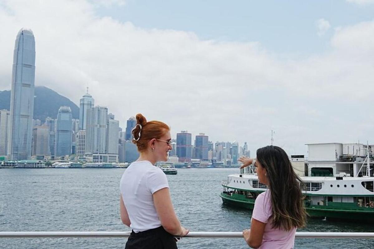 Dos mujeres de pie en una barandilla cerca del agua con barcos