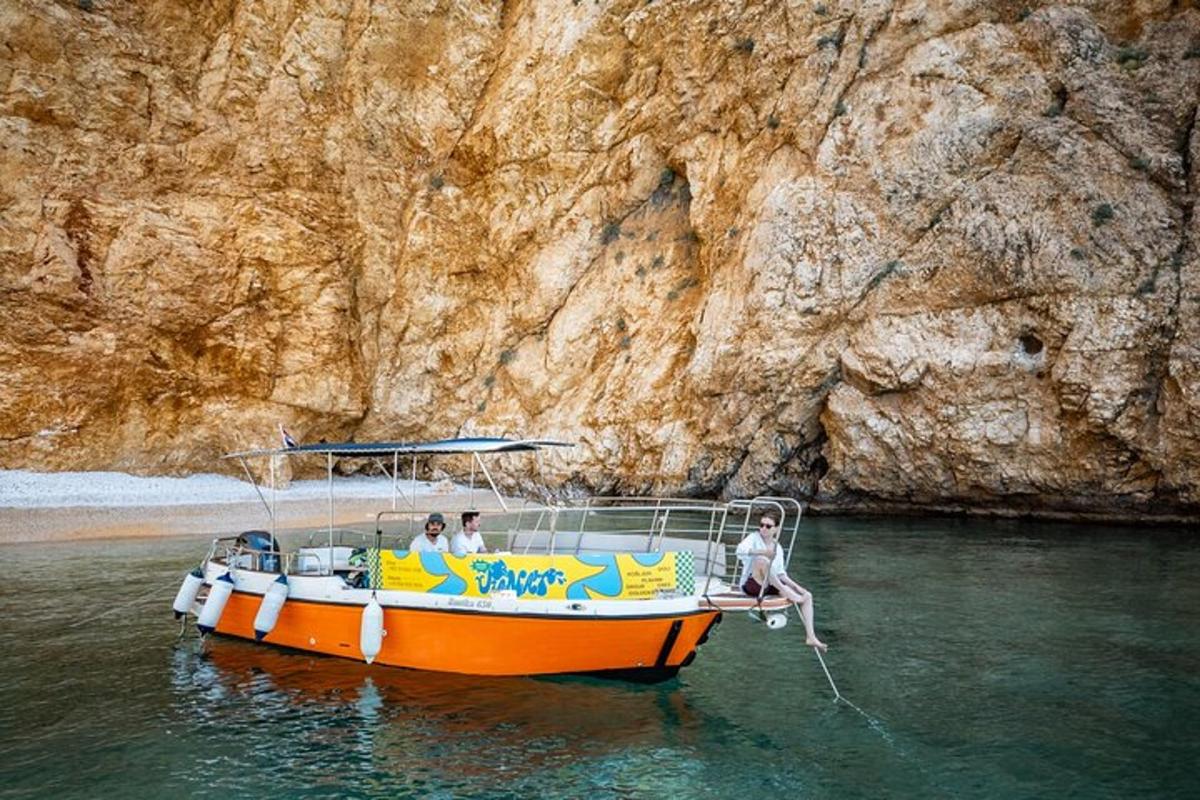 an orange boat on the water next to a cliff