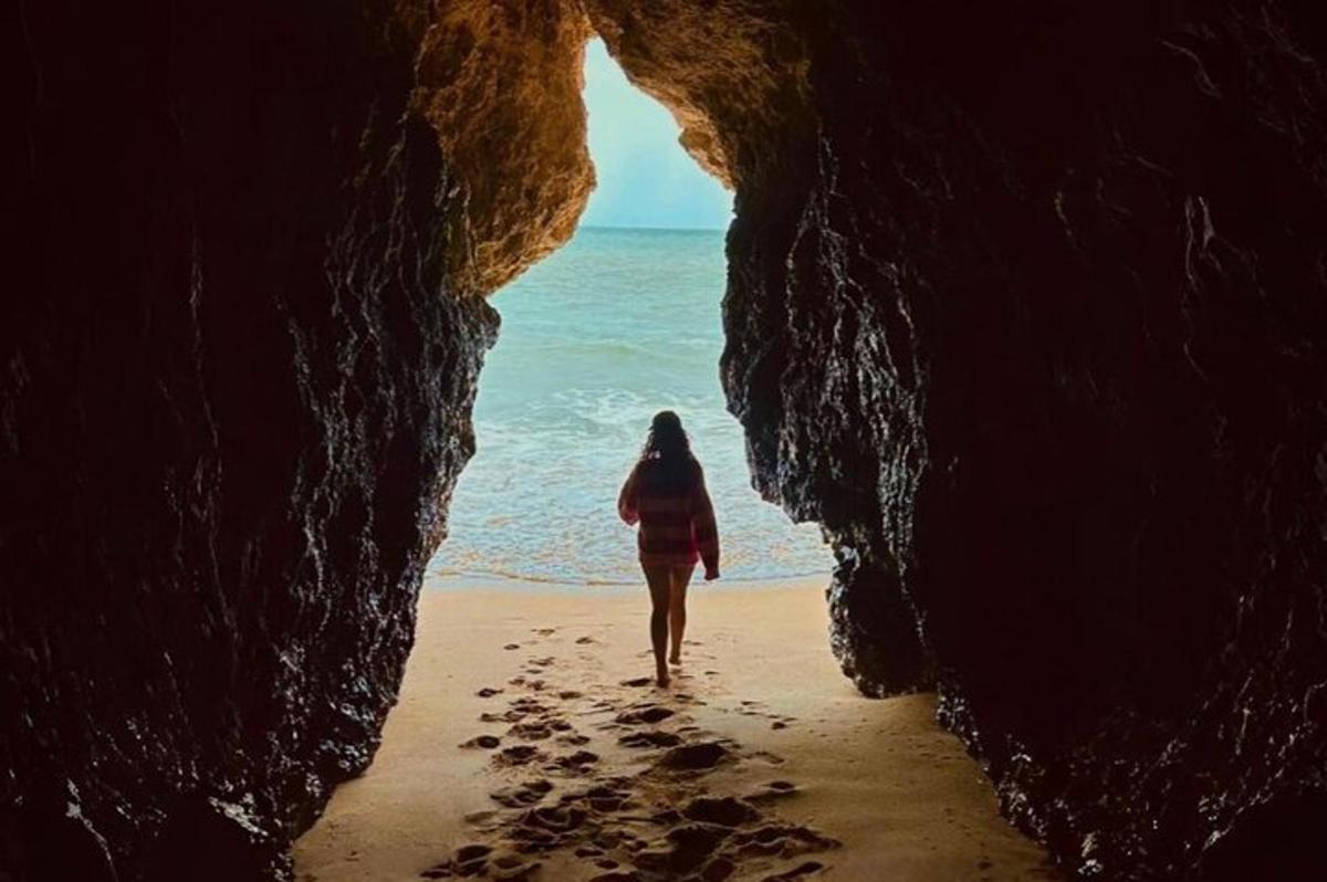 a woman walking through a cave on the beach