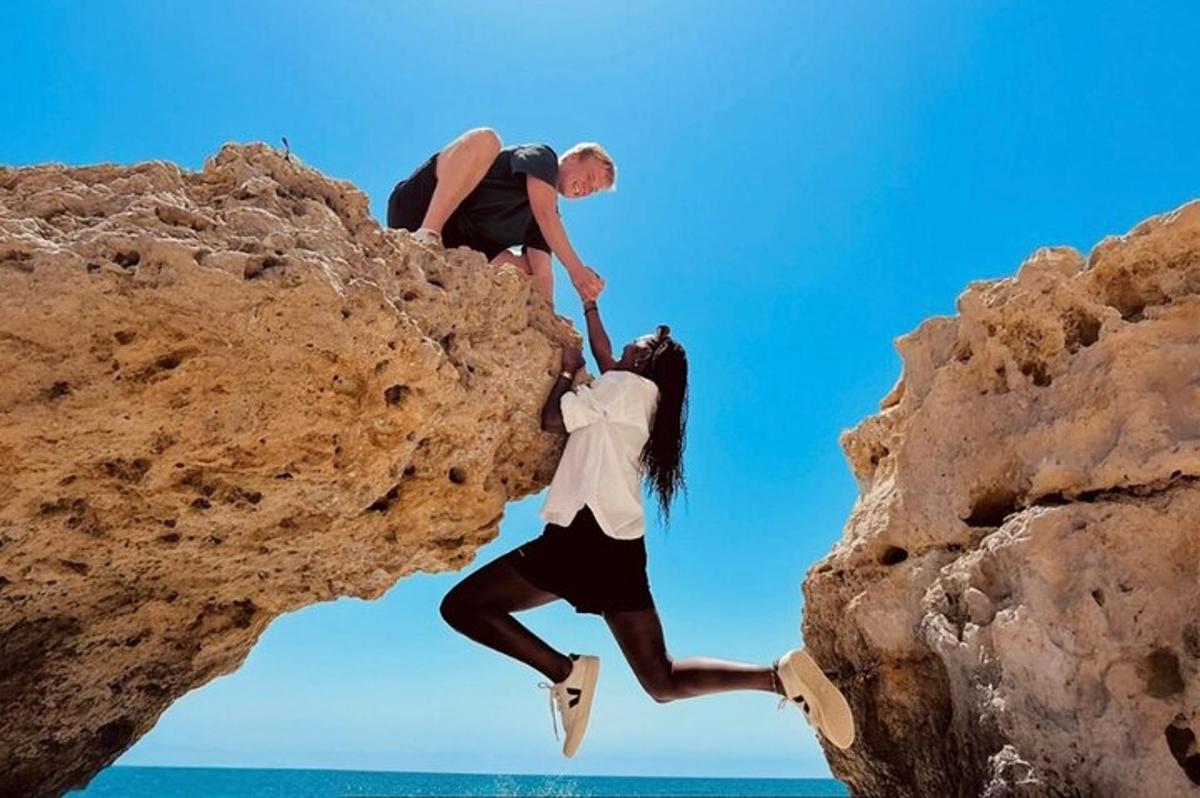 two people jumping off a rock on the beach