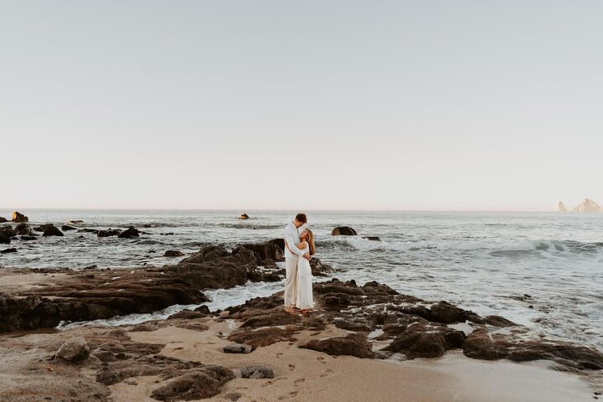 a bride and groom standing on the rocks on the beach