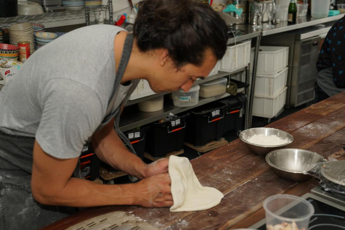 Un hombre en una cocina amasando masa sobre un mostrador.