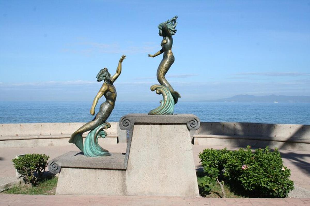 a statue of three mermaids on a wall near the ocean