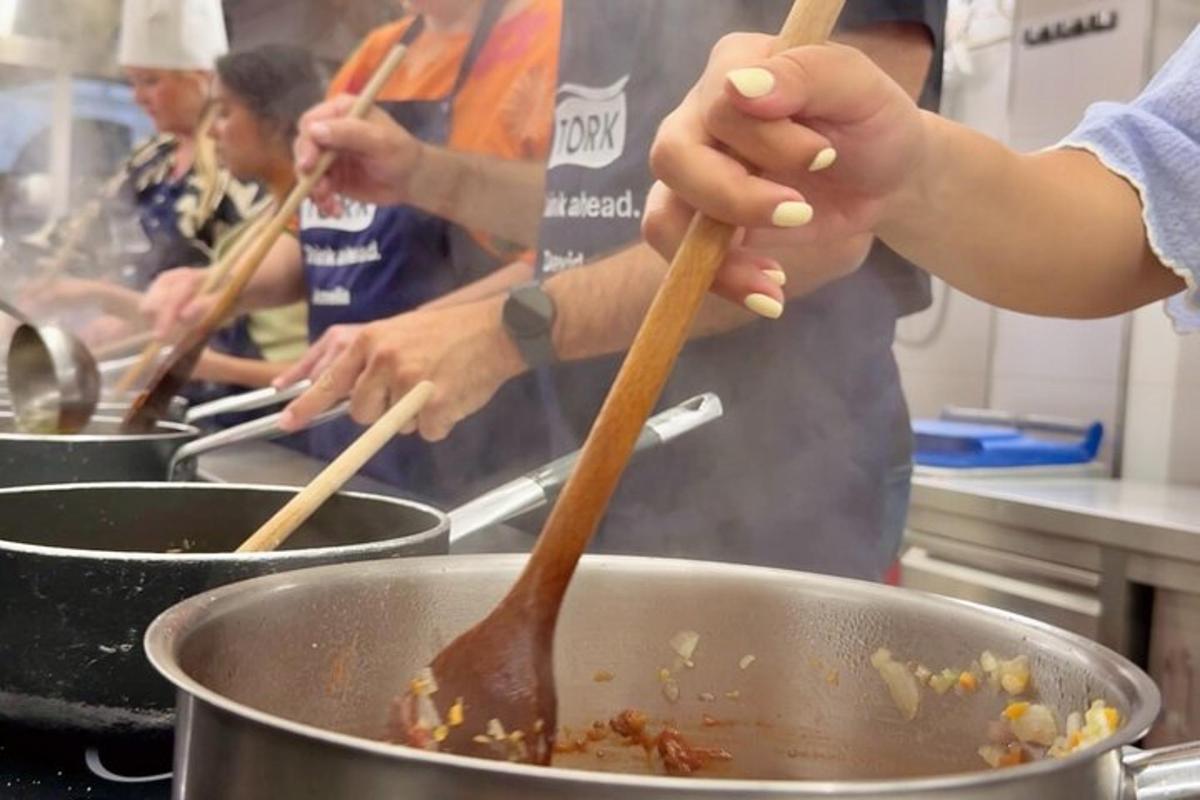 skupina lidí míchá jídlo v hrnci s dřevěnými tyčinkami