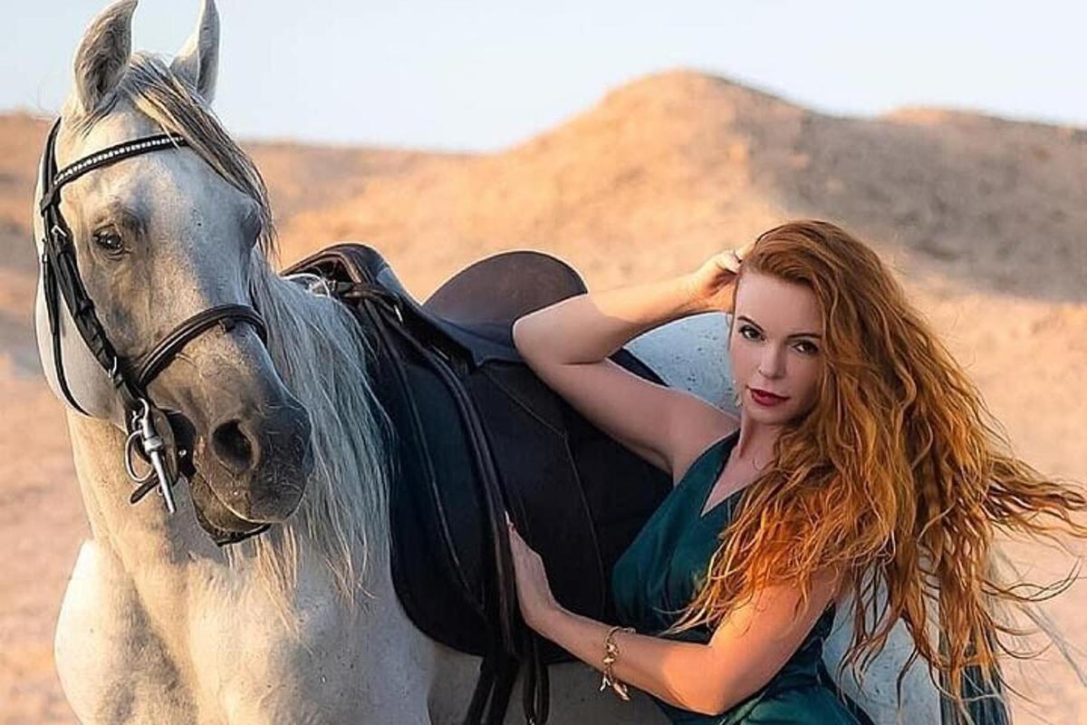 Una mujer joven está montando un caballo blanco