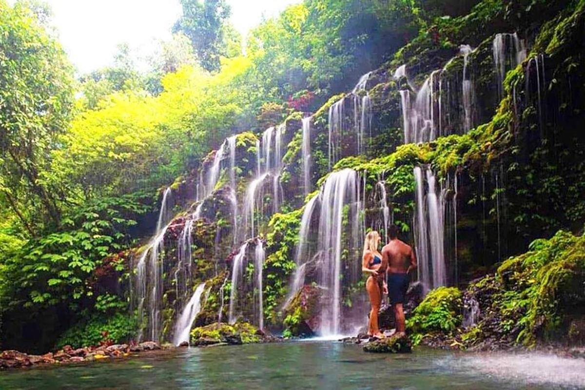 dua orang berdiri di sungai di depan air terjun