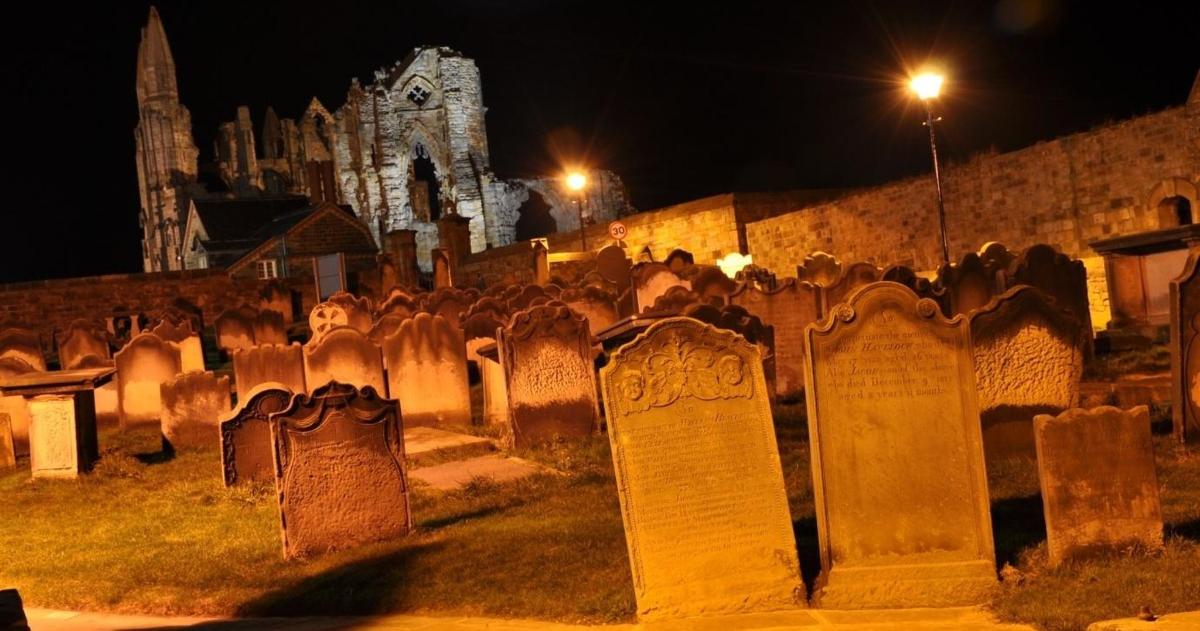 hřbitov v noci s hodinovou věží v pozadí