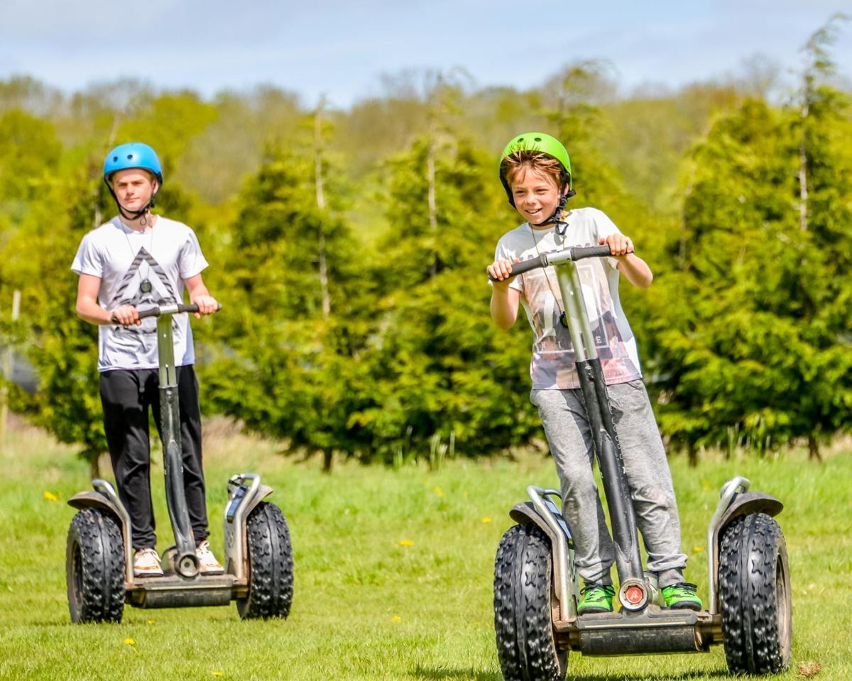 two young boys riding on electric scooters in a field