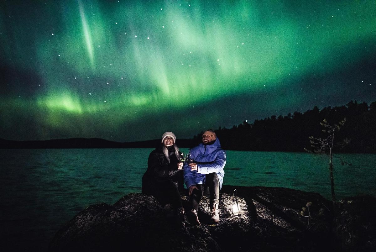 two people sitting on a rock under the northern lights