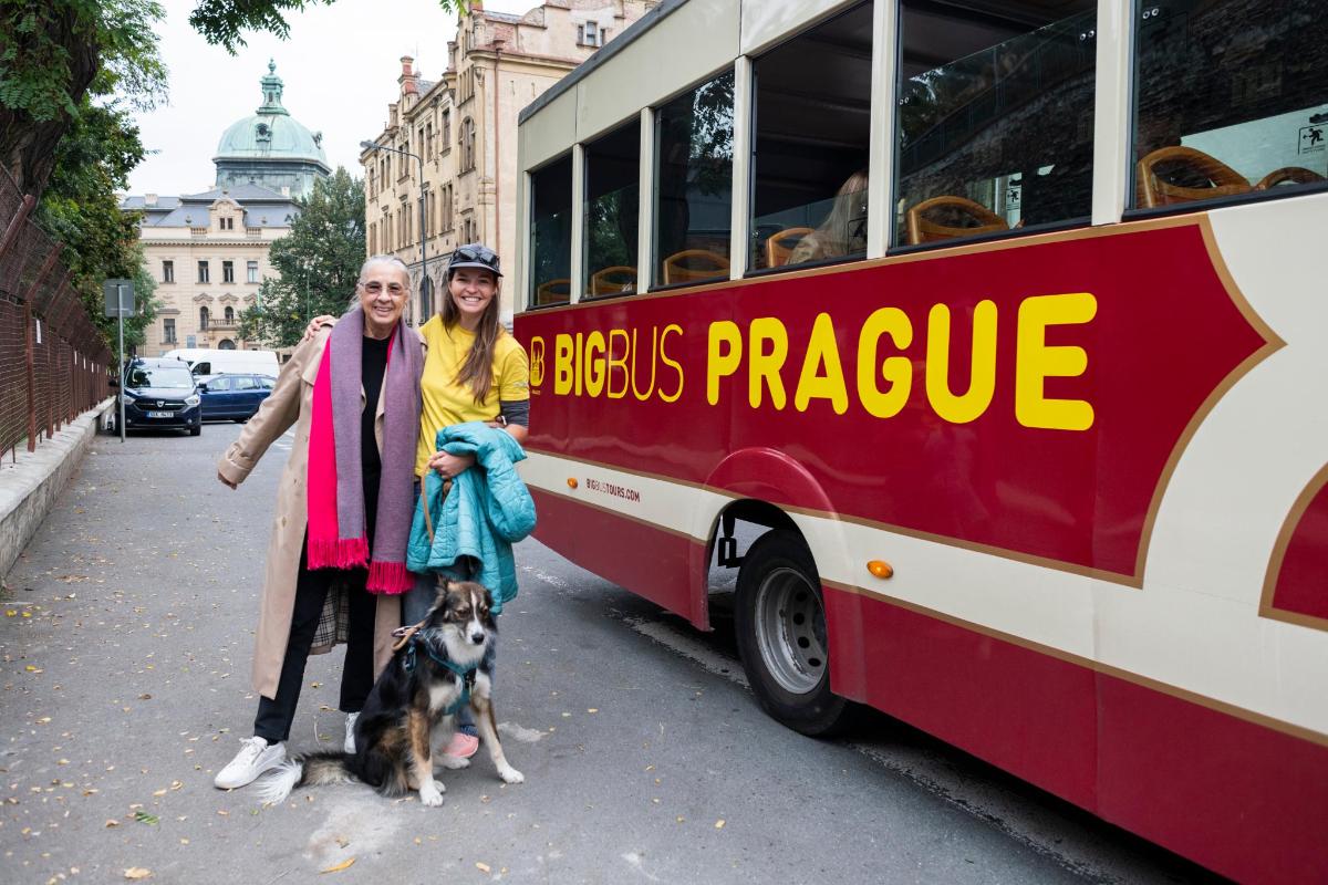 two people and a dog standing in front of a bus