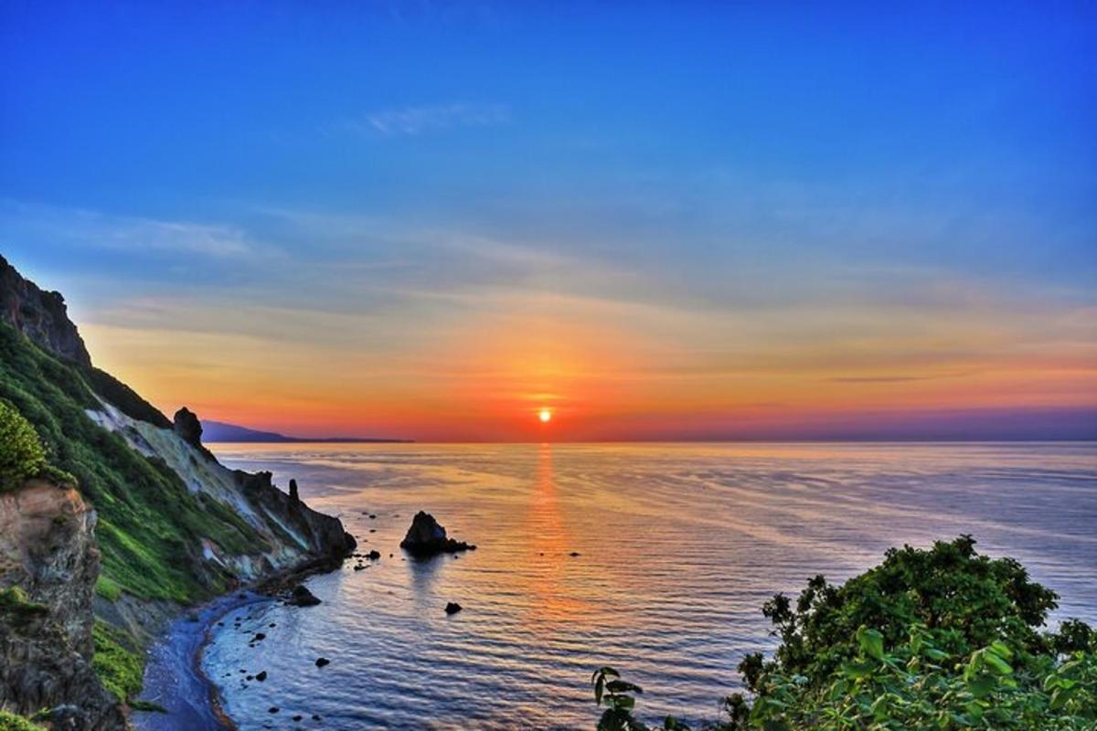a sunset over the ocean with rocks in the water