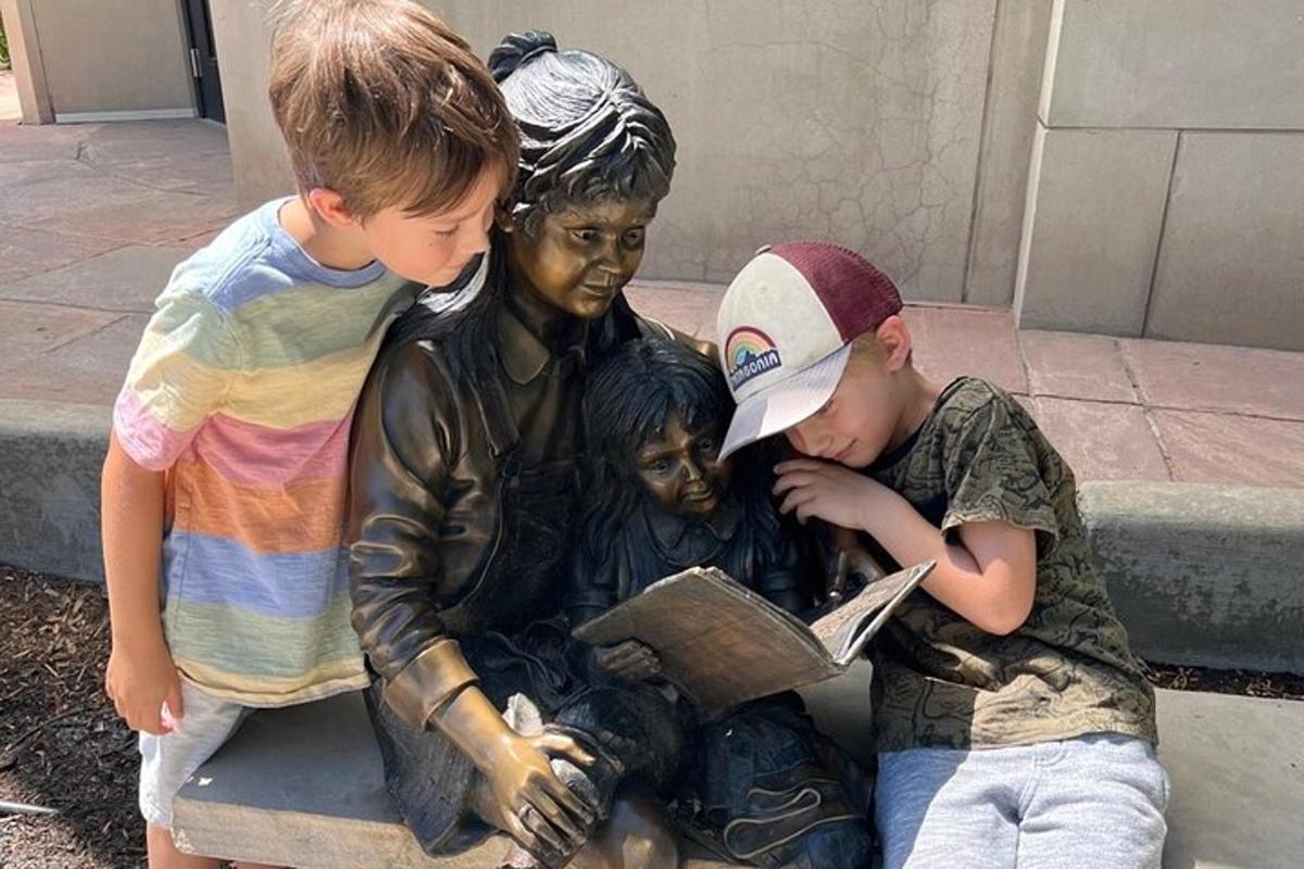 a group of children looking at a statue of a boy reading a book