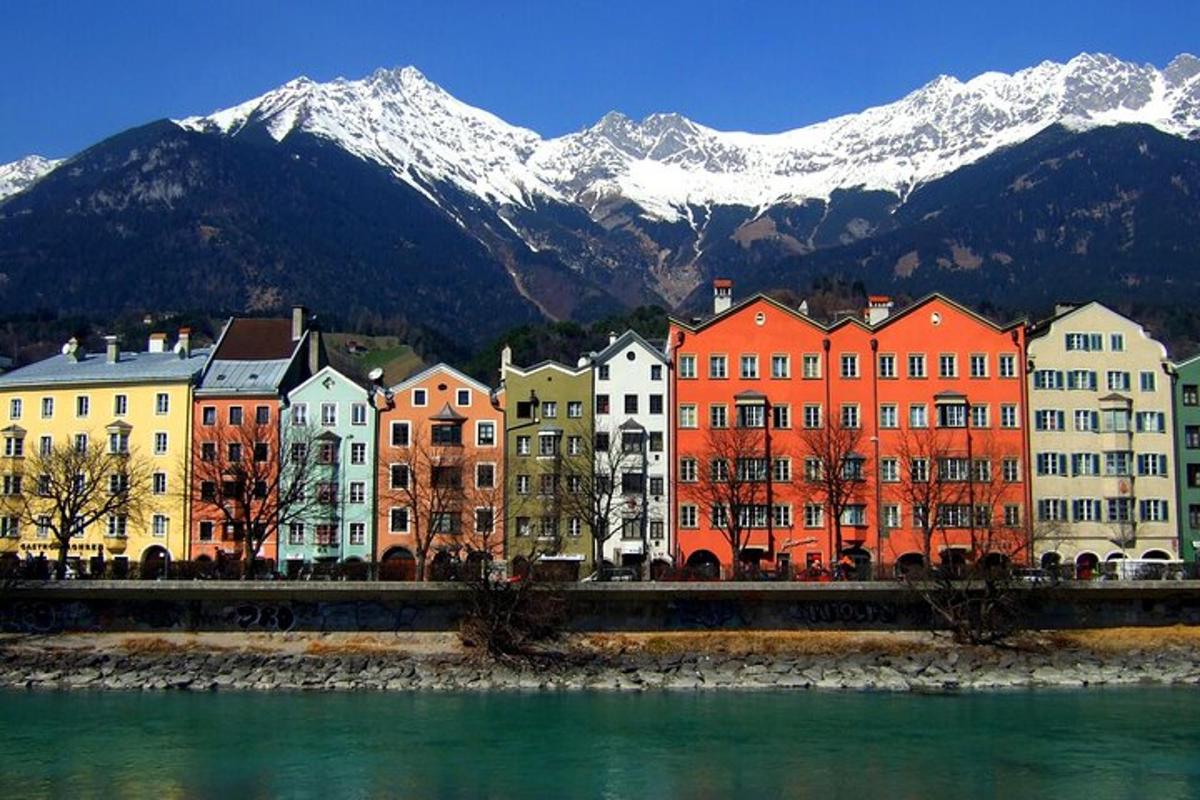 a group of buildings next to a river with snow covered mountains