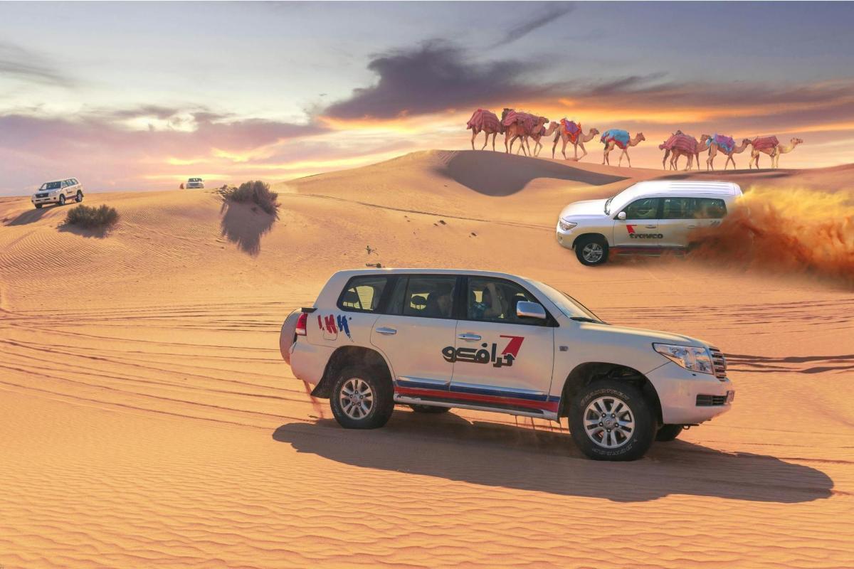 two trucks driving in the desert with camels