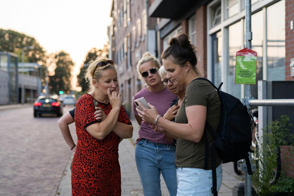 three women standing on a sidewalk looking at a cell phone
