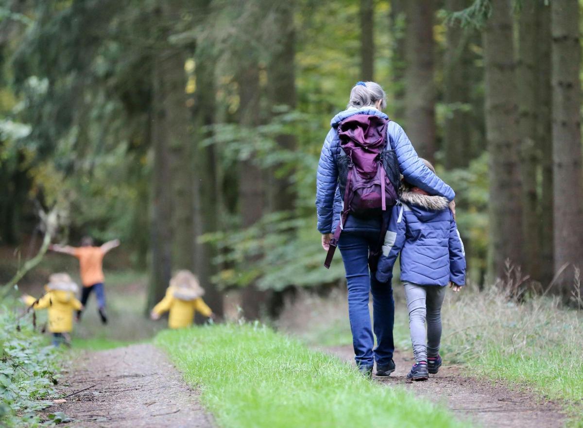 a woman and child walking down a path in the woods