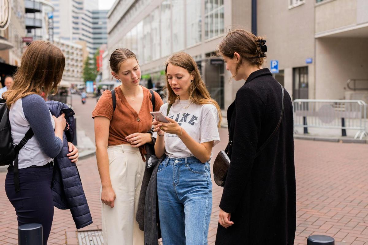 a group of women standing on a street looking at a cell phone