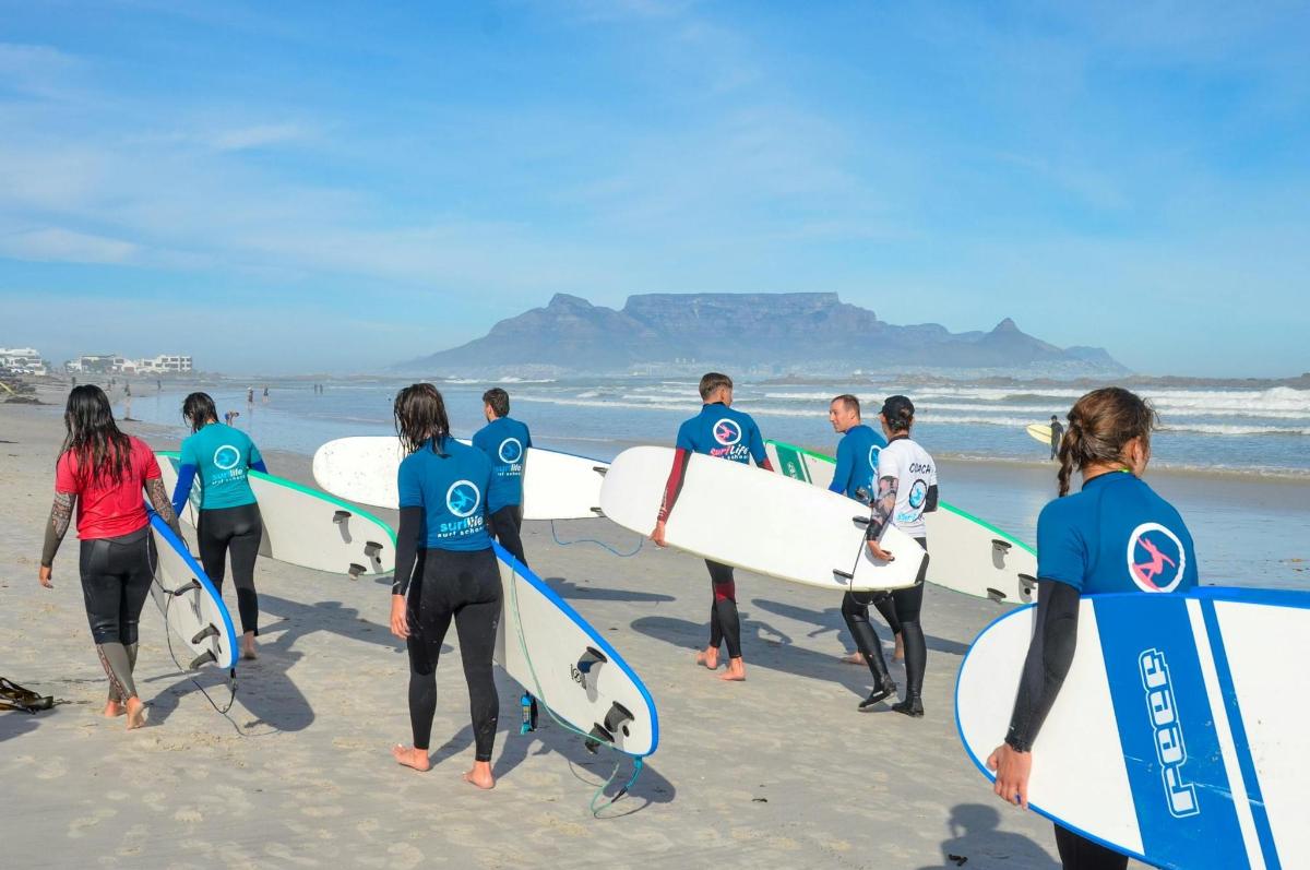 a group of people walking on the beach with surfboards