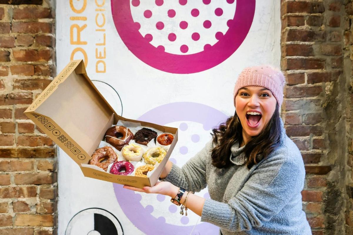 a woman is holding a box of donuts