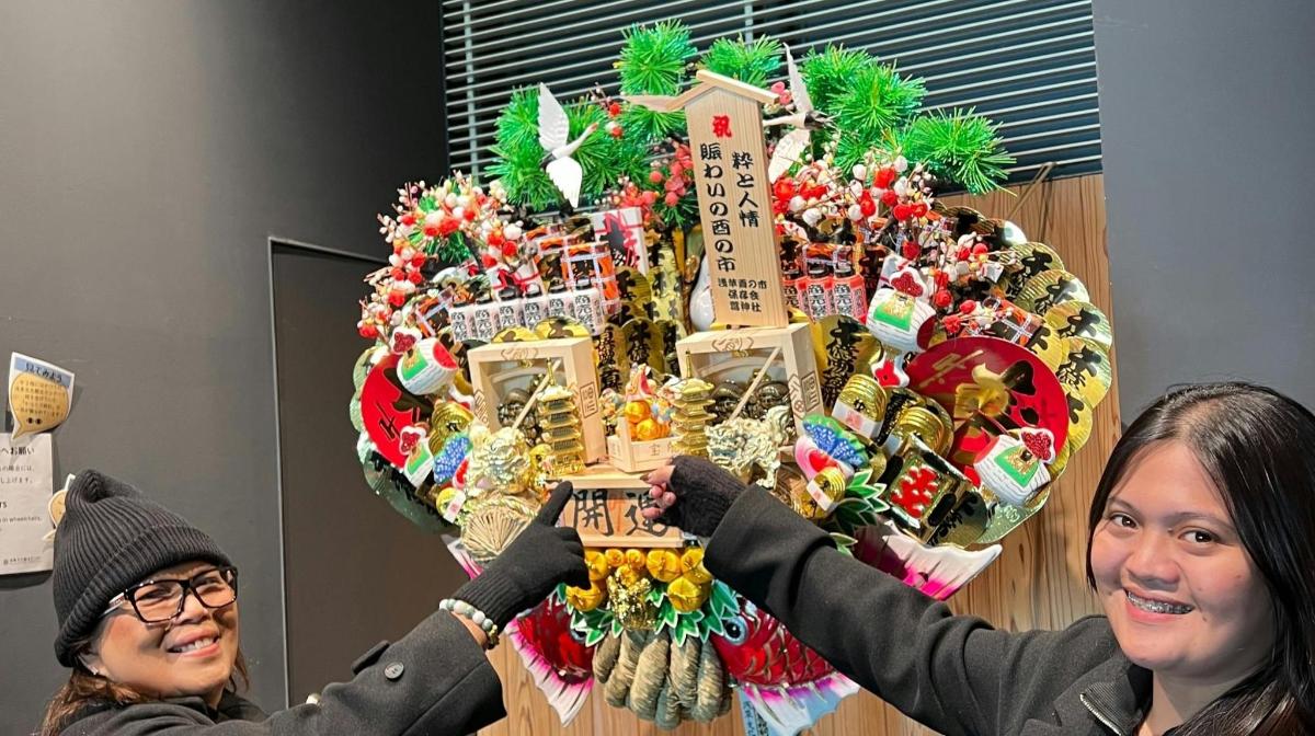 two women standing in front of a christmas wreath