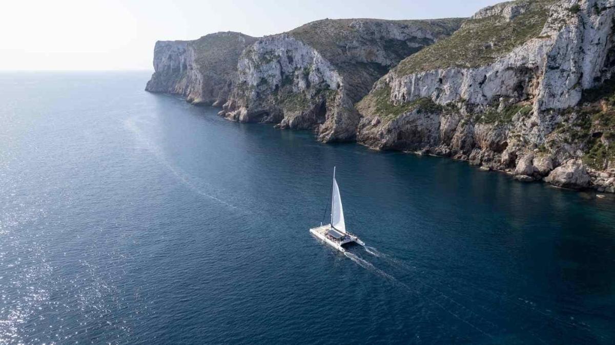 a sail boat in the water near a cliff