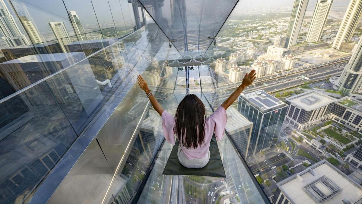 a woman sitting on the glass floor of a skyscraper