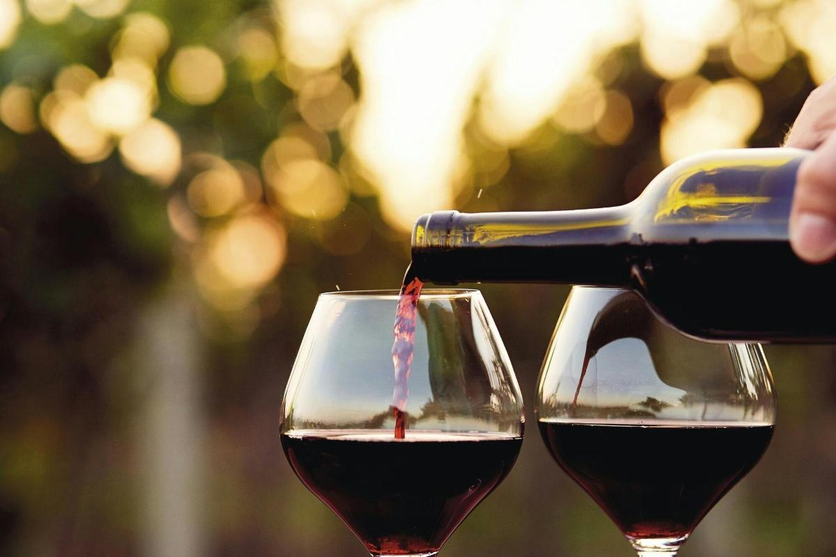 eine Person gießt Rotwein in zwei Weingläser