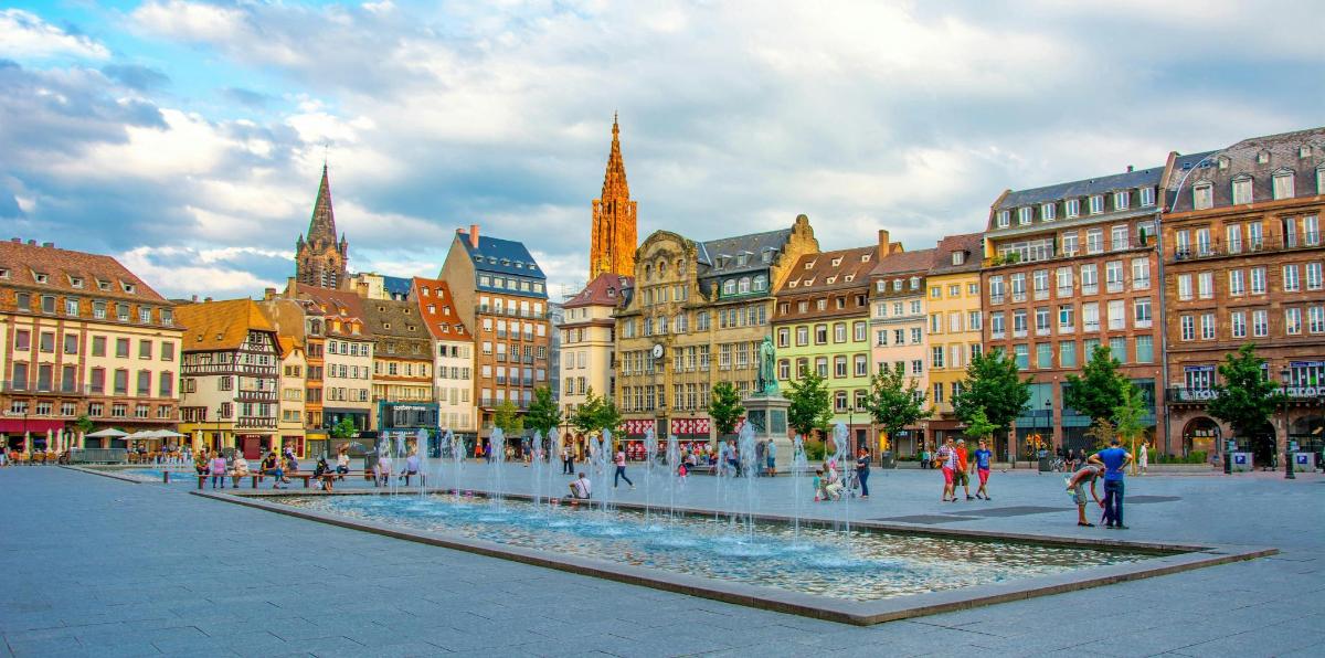 a city square with a fountain in front of buildings