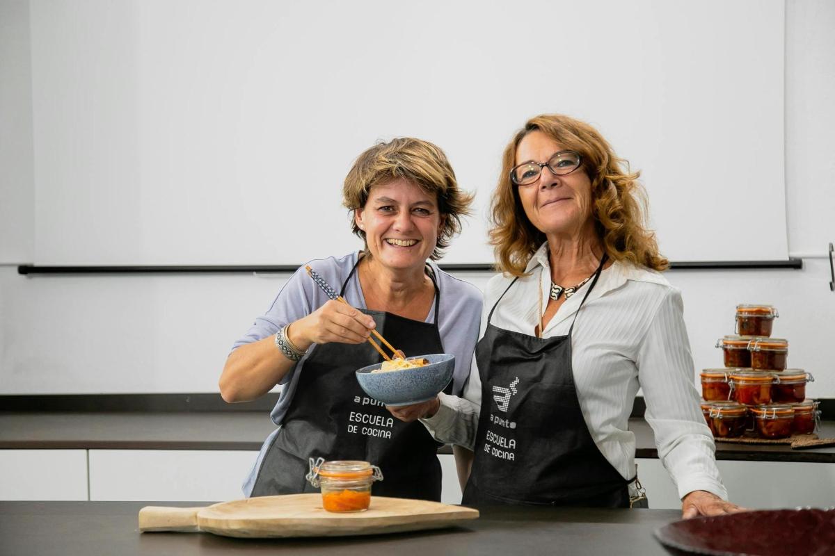 two women standing in a kitchen holding a bowl of food
