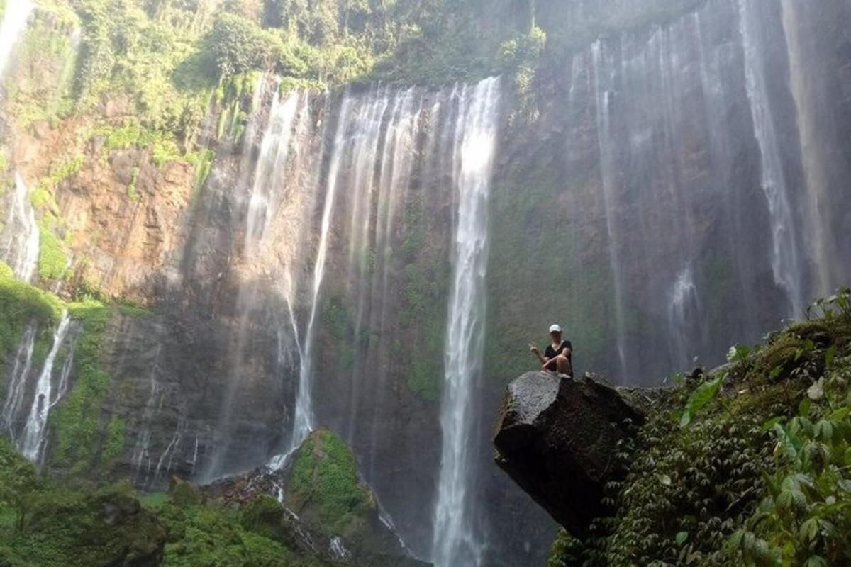 a man sitting on a rock in front of a waterfall