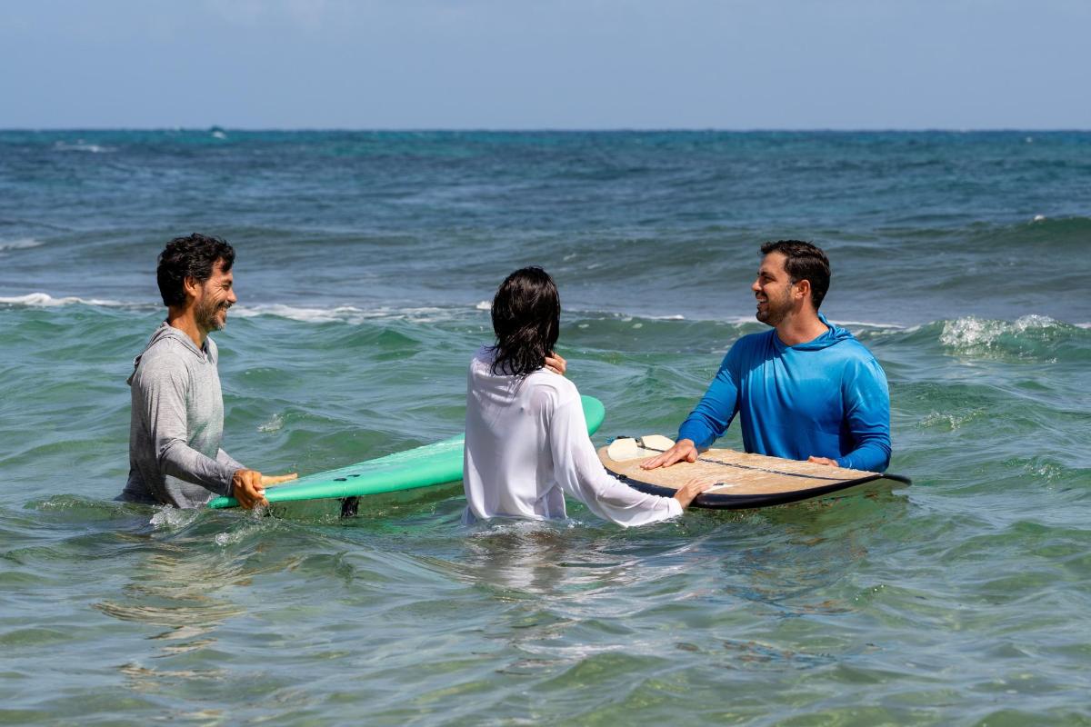 three people sitting on a surfboard in the ocean