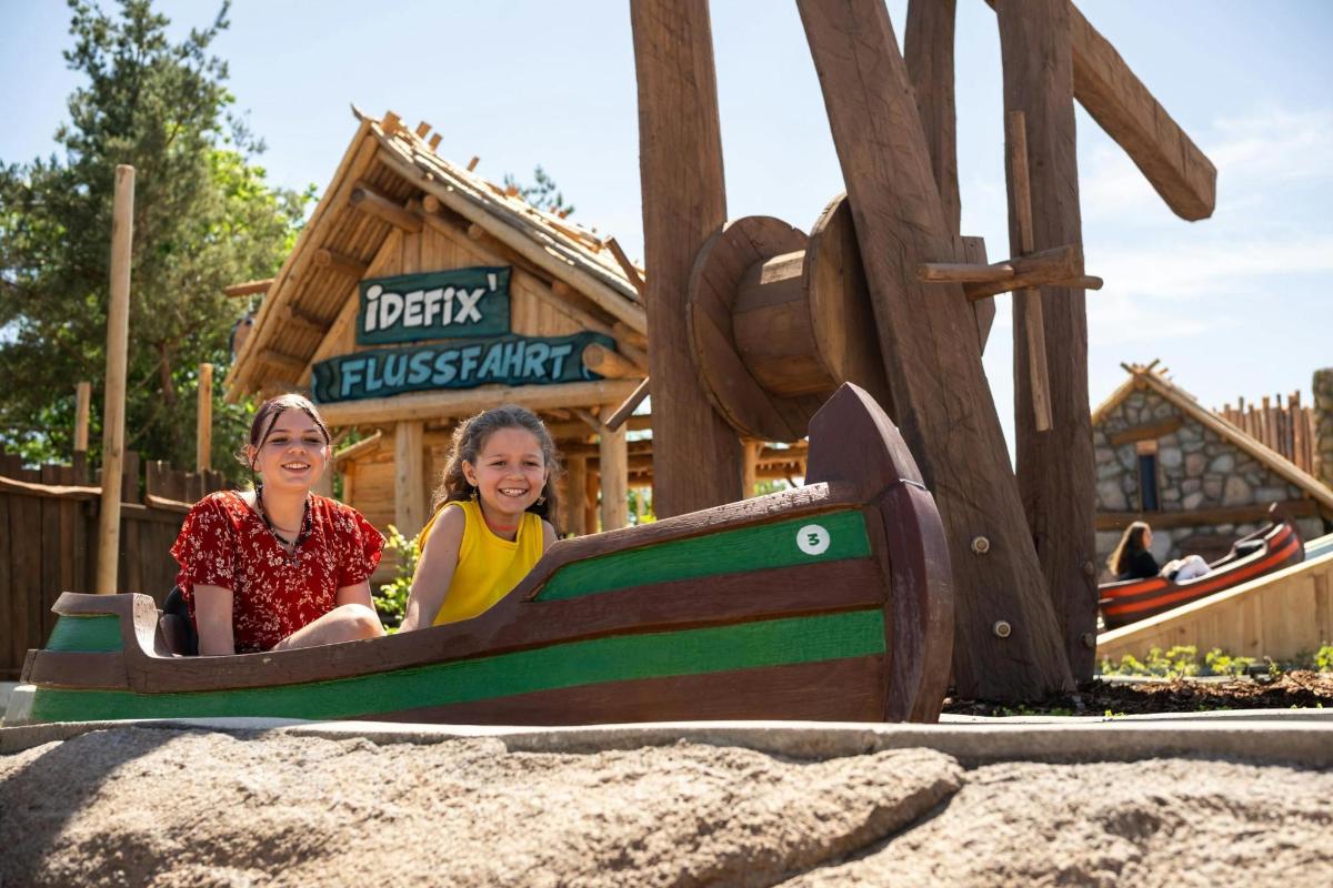 two girls sitting in a toy train at a playground