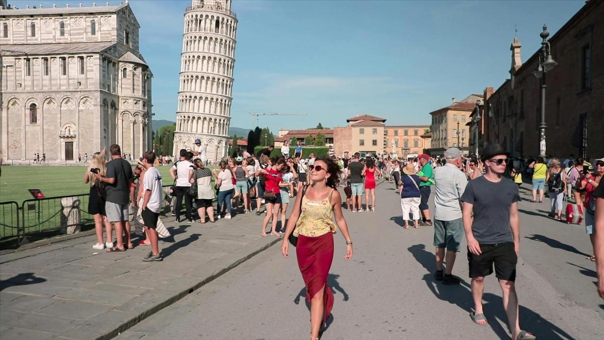a group of people walking down a street in front of the leaning tower