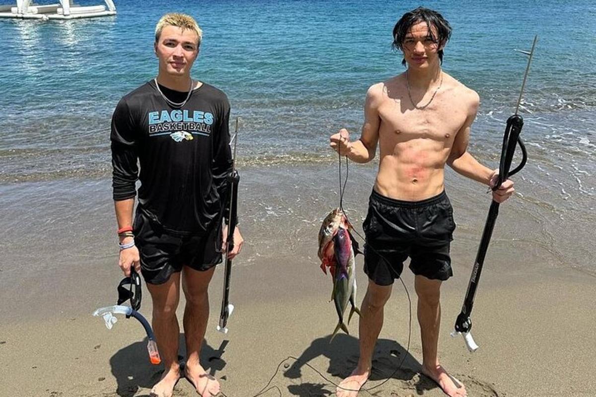two men standing on the beach holding fishing rods